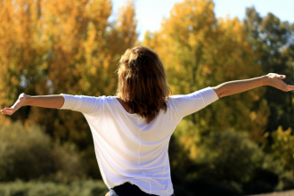 individual with arms extended, face towards sun